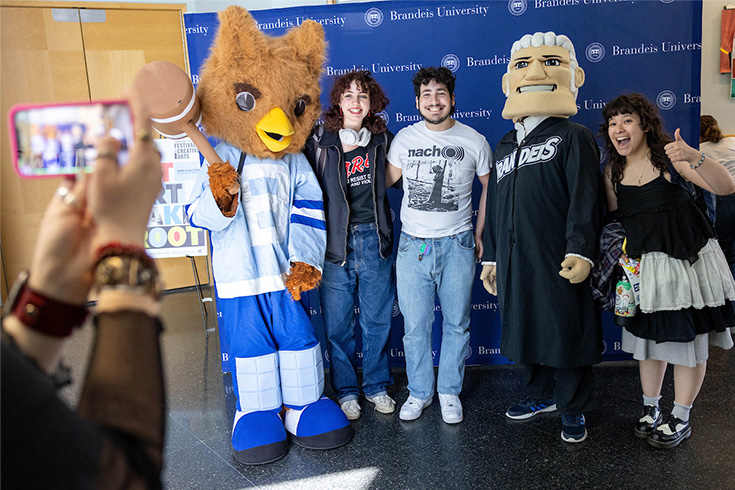 Three students pose with judge mascot and owl mascot against a blue backdrop