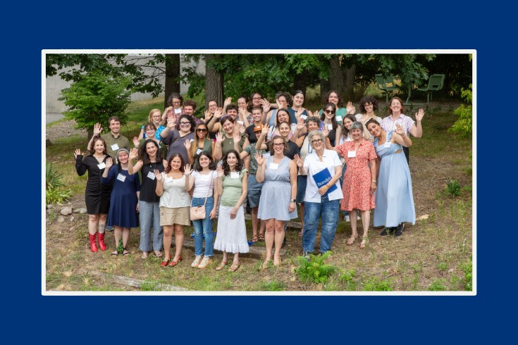 a large group of people standing together on a grassy hill, waving and smiling at the camera