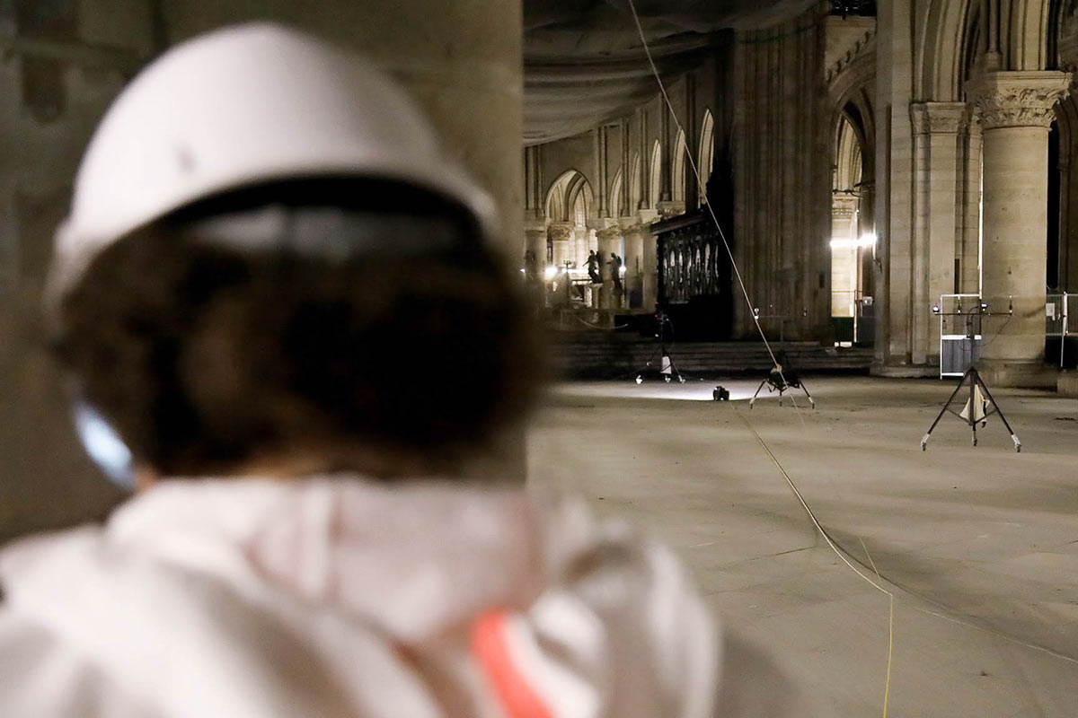 A person wearing white protective gear and a hard hat controls a remotely operated robot.