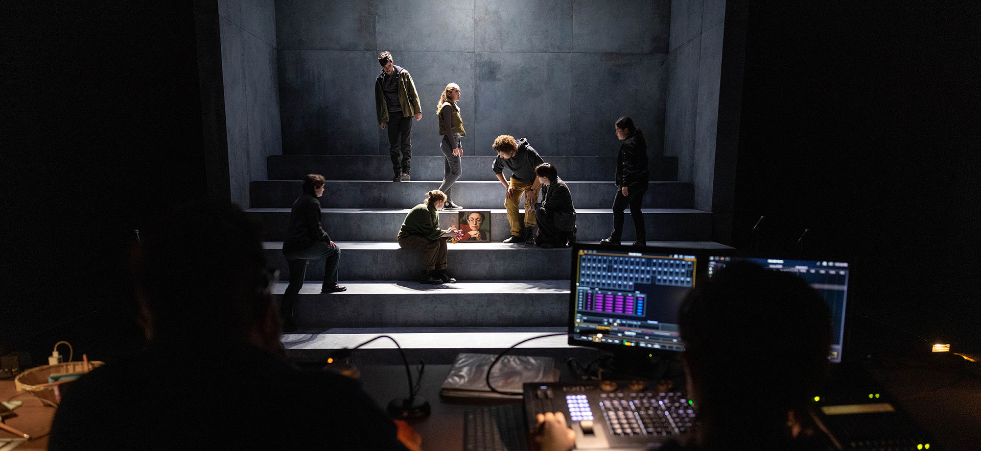 Students act on a stage while people in a lighting and sound booth look on.